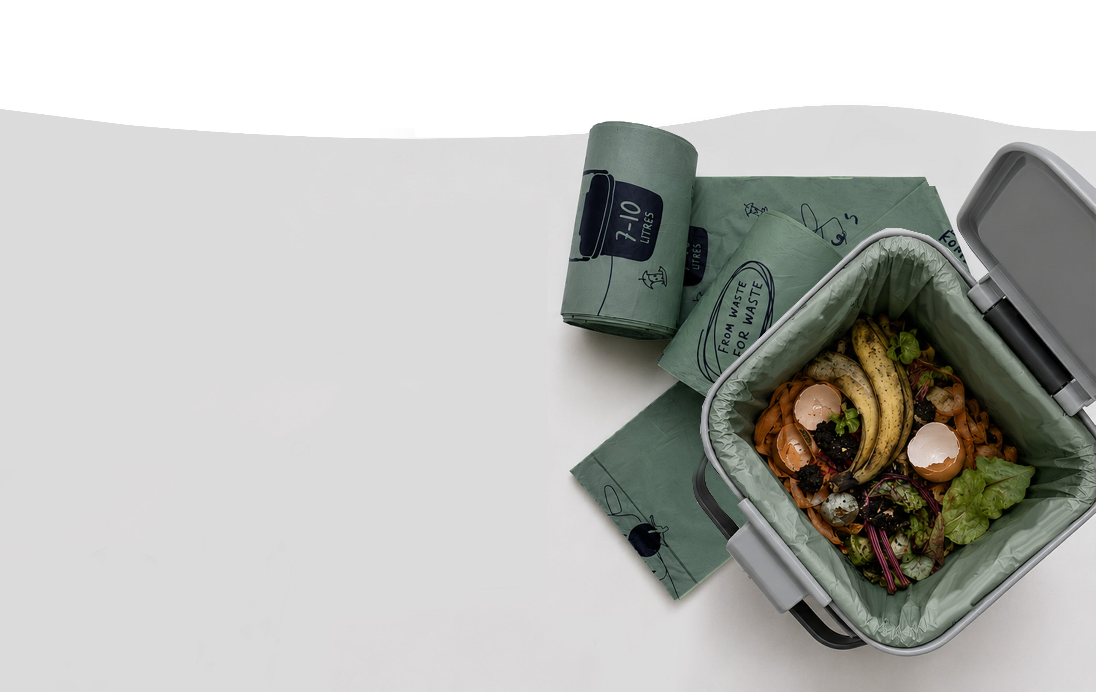 Kompost compostable kitchen caddy liner filled with food waste, with rolls of waste-potato-based caddy liners alongside.