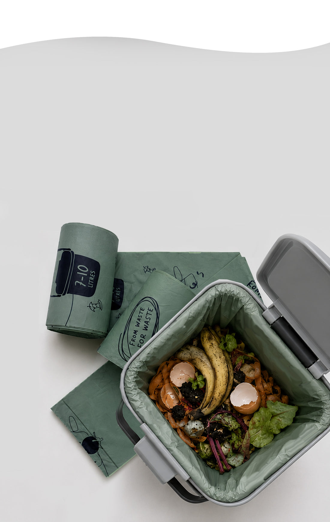 Kompost compostable kitchen caddy liner filled with food waste, with rolls of waste-potato-based caddy liners alongside.